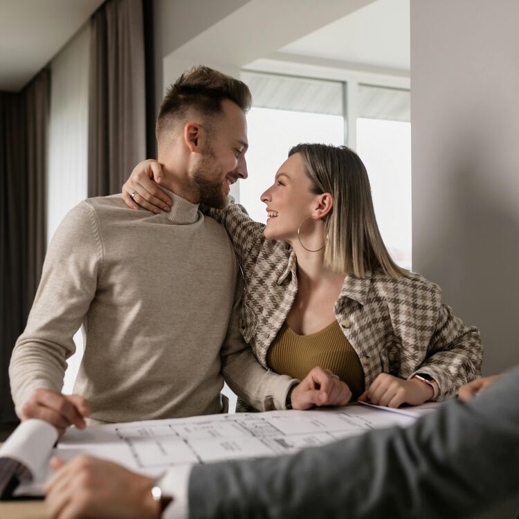 Happy couple embracing while looking over new home plans with their advisor.