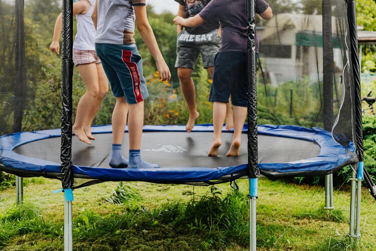 Children jumping and playing on a trampoline in the backyard.