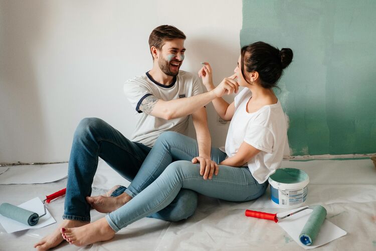 Couple painting a wall together and laughing while renovating their home.