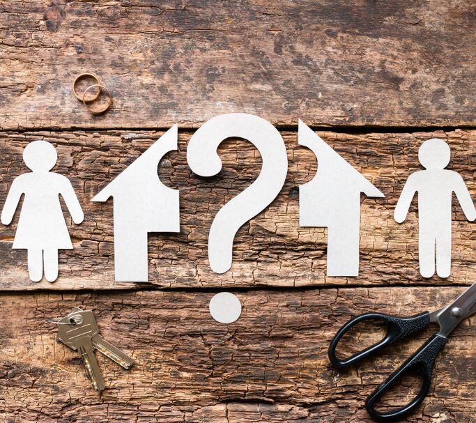 Paper cutouts of houses, people, and a question mark on wood, symbolizing separation and housing decisions